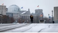 A cyclist drives on a snowy street between the Reichstag building (L) housing the Bundestag (lower house of parliament) and the Chancellery (R) in Berlin's governmental district on November 29, 2023. (Photo by Odd Andersen / AFP)