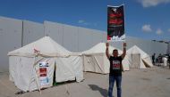 A man lifts a placard near tents set up by volunteers and NGO workers along the Egyptian side of the Rafah border crossing, demanding clearance for an aid convoy to enter the Gaza Strip, on October 19, 2023. (Photo by Kerolos Salah / AFP)