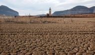 This photograph taken on January 15, 2024 shows the dry soil next to the low water-level reservoir of Sau with in background Sant Roma de Sau church, in the province of Girona in Catalonia. Catalonia struggles with historic drought for three years, with some residents already experiencing water restrictions in their daily life. (Photo by LLUIS GENE / AFP)