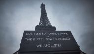 This photograph taken on February 19, 2024, in central Paris, shows a board informing visitors that the Eiffel Tower, viewed in the background, is closed as staff go on strike, over the financial management of the monument by the city, closing the monument to the public during the second week of the French school holidays. (Photo by Kiran RIDLEY / AFP)
