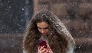 A young woman looks at her smartphone during snowfall in Kyiv, on March 12, 2024, amid the Russian invasion of Ukraine. (Photo by Anatolii STEPANOV / AFP)
