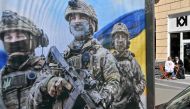 A couple sits outside a cafe next to a military recruiting poster in Kyiv, on April 9, 2024, amid Russia's invasion on Ukraine. (Photo by Sergei Supinsky / AFP)
