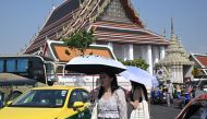 (Files) Tourists shield themselves from the sun with umbrellas to combat the heat outside Wat Pho Buddhist temple in Bangkok on April 1, 2024. (Photo by Lillian Suwanrumpha / AFP)
