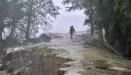 A man walks on a damaged embankment along the Sonatola river during heavy rainfall in Patuakhali on May 27, 2024, following the landfall of Cyclone Remal in Bangladesh. Photo by Munir Uz Zaman / AFP.