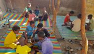 Children sit together sharing a large bowl of food, as Sudanese families host internally displaced people coming from the central Sudanese state of Gezira to the eastern Sudanese city of Gedaref on June 3, 2024. Photo by Ebrahim HAMID / AFP.