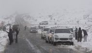 People stand next to a road taking pictures of the unusually heavy snowfall on the mountains around the Bo-Swaarmoed Pass near Ceres on July 8, 2024. (Photo by RODGER BOSCH / AFP)

