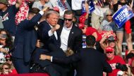 File: Republican candidate Donald Trump is seen with blood on his face surrounded by secret service agents as he is taken off the stage. (Photo by Rebecca Droke / AFP)