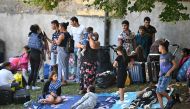 Refugees sit on the pavement close to their former shelter in Kocs village, about 70 km north-west from the Hungarian capital Budapest, on August 21, 2024. (Photo by Attila 
Kisbenedek / AFP)
 
