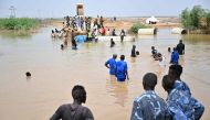 Sudanese army soldiers look on as people use a boat in an inundated area in Tokar in the Red Sea State, following recent heavy flooding in eastern Sudan, on September 5, 2024. Photo by AFP