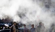 Pedestrians wait to cross a road as a cooling water mist is sprayed from nearby pipes in Busan on September 4, 2024. (Photo by ANTHONY WALLACE / AFP)
