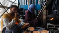 A Palestinian man eats flat bread made with ground lentils during a flour shortage, as woman bakes a new batch in the Jabalia camp for refugees in the northern Gaza Strip on May 6, 2025. Photo by Omar AL-QATTAA / AFP