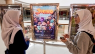 This picture taken on April 21, 2025 shows two teenagers speaking next to a poster of the animated film Jumbo at a cinema in Bekasi, West Java. (Photo by Bay Ismoyo / AFP) 