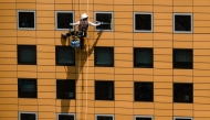 Photo used for representational purposes. A window cleaner uses a squeegee while rappelling down a commercial building in Seoul on June 23, 2025. (Photo by Anthony WALLACE / AFP)