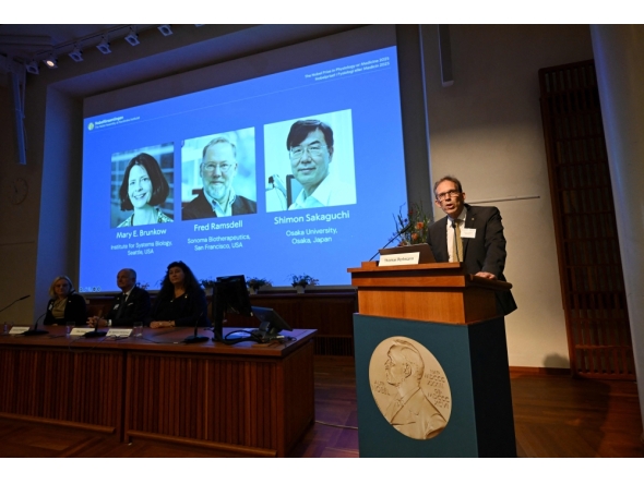 Nobel Committee Secretary General Thomas Perlmann (R) addresses journalists in front of a screen displaying the portraits of (L-R) Mary E Brunkow, Fred Ramsdell and Shimon Sakaguchi during a press conference. (Photo by Jonathan Nackstrand / AFP)