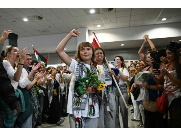 Swedish climate campaigner Greta Thunberg raises her fist, upon arrival alongside activists who were sailing aboard vessels from the Gaza-bound aid flotilla before being stopped and detained by Israeli forces, greeted by a crowd of supporters, at the arrivals area of Athens International Airport on October 6, 2025. (Photo by Aris Messinis / AFP)