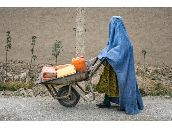 An Afghan burqa-clad woman pushes a wheelbarrow loaded with empty water canisters as she walks along a street in the Koshkak area of the Balkh province on October 5, 2025. (Photo by Atif Aryan / AFP)
