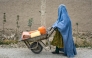 An Afghan burqa-clad woman pushes a wheelbarrow loaded with empty water canisters as she walks along a street in the Koshkak area of the Balkh province on October 5, 2025. (Photo by Atif Aryan / AFP)
