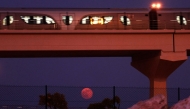 The full moon rises on the horizon as a metro train passes in Doha on October 7, 2025. (Photo by Karim Jaafar / AFP)