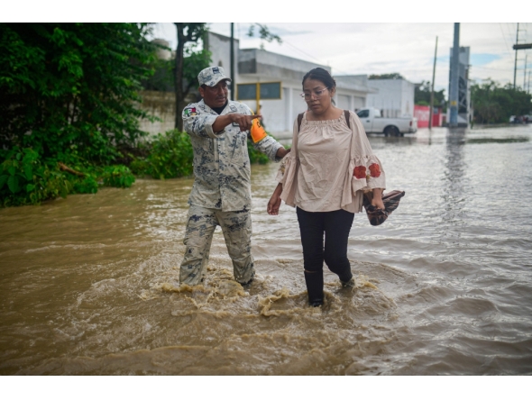 A member of the National Guard helps evacuate a woman through a flooded street following heavy rains in Poza Rica, Veracruz state, Mexico, on October 10, 2025. (Photo by Marco Antonio Perez / AFP)