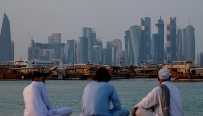 People sit along the corniche facing traditional dhow boats anchored in front of the Doha skyline on October 29, 2025. (Photo by Karim Jaafar / AFP)