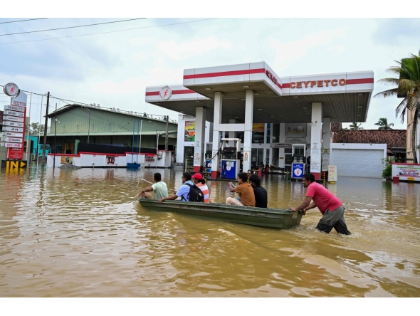 People ride a boat across a flooded street in Ambatale on the outskirts of Colombo on November 29, 2025. (Photo by Ishara S. KODIKARA / AFP)