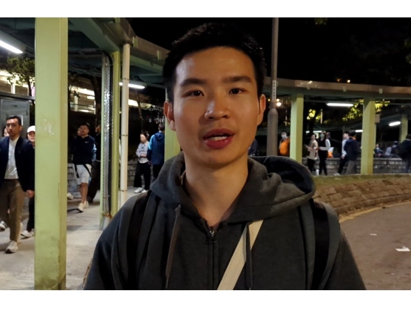 Miles Kwan, a 24-year-old student, speaks to AFP while handing out flyers outside a train station in Hong Kong's Tai Po district on November 28, 2025. (Photo by Holmes Chan / AFPTV / AFP)