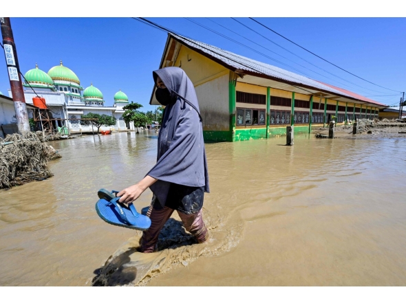 A woman walks past a mosque in a flooded area in Meureudu, Pidie Jaya district in Indonesia's Aceh province on November 30, 2025. (Photo by CHAIDEER MAHYUDDIN / AFP)
