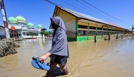 A woman walks past a mosque in a flooded area in Meureudu, Pidie Jaya district in Indonesia's Aceh province on November 30, 2025. (Photo by CHAIDEER MAHYUDDIN / AFP)

