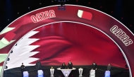 Qatar's flag is displayed on a screen during the draw for the 2026 FIFA Football World Cup taking place in the US, Canada and Mexico, at the Kennedy Center, in Washington, DC, on December 5, 2025. (Photo by Roberto SCHMIDT / AFP)
