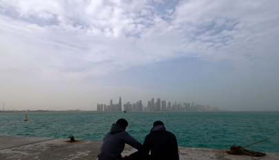 Visitors sit along the waterfront on a foggy day at the Corniche area facing the high-rise buildings in the West Bay district, in Doha on January 15, 2026. (Photo by Karim JAAFAR / AFP)

