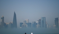 People look at the skyline covered in fog in Doha on February 9, 2026. (Photo by Mahmud HAMS / AFP)

