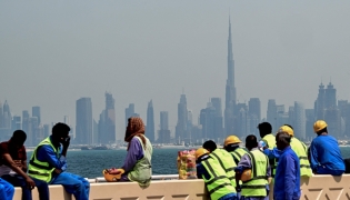 (Files) Workers sit on a wall against the backdrop of the Dubai city skyline on March 11, 2026. (Photo by Giuseppe Cacace / AFP)