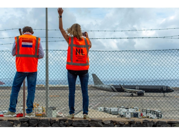 Representatives from the Netherlands embassy wave as a plane bound for the Netherlands carrying passengers evacuated from the Dutch-flagged hantavirus-stricken cruise ship MV Hondius prepares to take off from the Tenerife Sur-Reina Sofia airport on the island of Tenerife in Spain's Canary Islands on May 10, 2026. (Photo by Antonio Sempere / AFP)