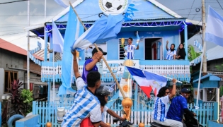 Argentina fan and fisherman Muhammad Yusuf (back C) holds a replica of the World Cup trophy as football fans pass his house, painted in the colours of the Argentine national team in Indonesia's West Sulawesi on June 11, 2026. (Photo by Muhammad Salim / AFP)
