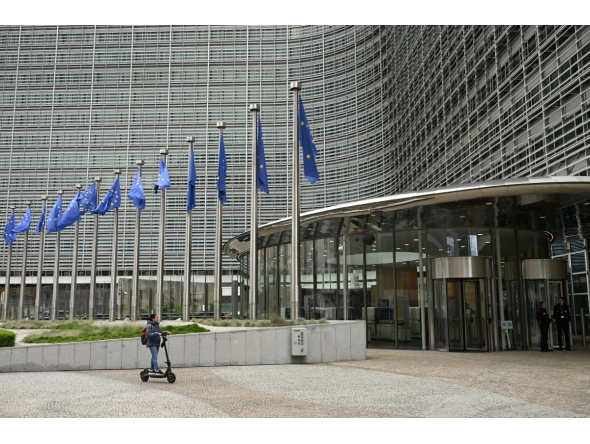 A woman rides an electric scooter past the Berlaymont building, the EU Commission headquarters, in Brussels on June 9, 2026. (Photo by Nicolas Tucat / AFP)

