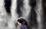 A woman cools off under a mist sprayer during the annual street music festival 'Fete de la Musique' while taking part in a heatwave in Bordeaux, southwestern France on June 21, 2026. (Photo by ROMAIN PERROCHEAU / AFP)
