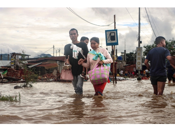 Residents wade through a flooded street near an overflowing river after heavy rains at Nambol in Bishnupur district, in India's northeastern state of Manipur on July 22, 2026. (Photo by Vishma Ahanthem / AFP)