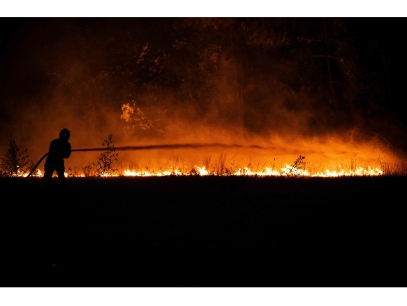 A firefighter sprays water on a burning forest close to a residential area during a wildfire near Lege-Cap-Ferret, southwestern France, on July 23, 2026. (Photo by Julien De Rosa / AFP)