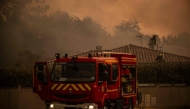 Firefighters spray water with a hose from the roof of a house during a wildfire near Lege Cap Ferret, southwestern France on July 23, 2026. (Photo by Julien De Rosa / AFP)
 
