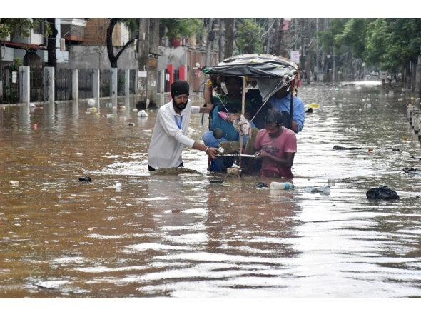 Residents wade through a flooded street following heavy monsoon rains in Guwahati on August 4, 2026. (Photo by Biju BORO / AFP)