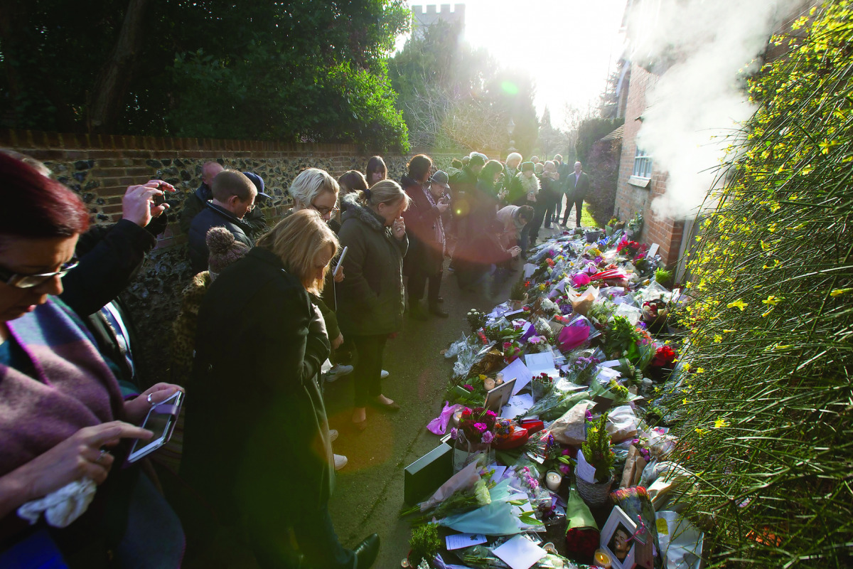 People gather and pause outside the home of British singer George Michael where tributes of flowers, messages and candles have been piled in the village of Goring, southern England, yesterday.