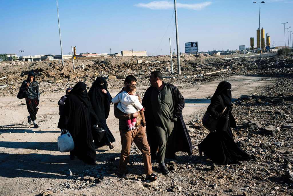Iraqis walk past an Islamic State (IS) group sign in the newly liberated part of eastern Mosul on January 17, 2017, during an ongoing military operation against the jihadists.   AFP / Dimitar DILKOFF

