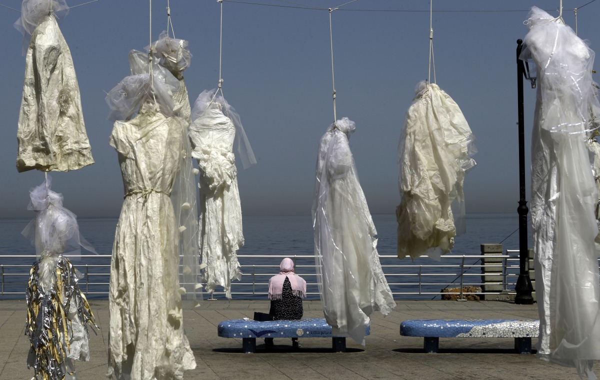 A veiled woman sitting on a bench near an installation of wedding dresses by Lebanese artist Mireille Honein and Abaad NGO at Beirut's Corniche, denouncing the article 522 of Lebanon's penal code allowing rapists who marry their victims to go free, in thi