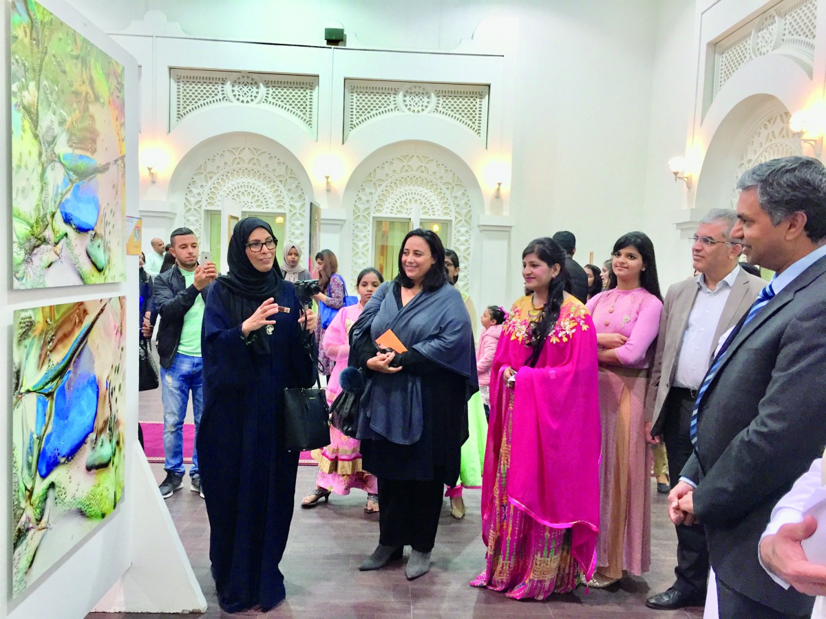 Qatari artist Moudhi Al Hajri (left) explains about her works on display while Indian Ambassador P Kumaran (right), MAPS Qatar President and Founder, Rashmi Agarwal (middle) and other artists and guests look on at the opening of “The Colours of Desert Ser