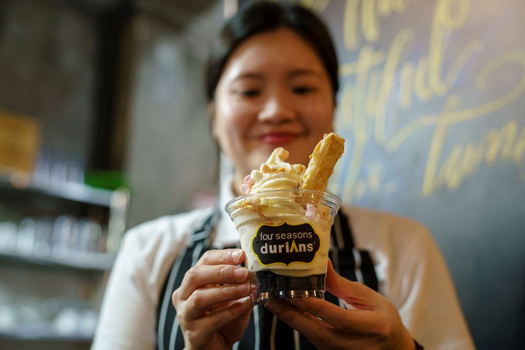 This photo taken on January 24, 2018 shows a staff member holding up a cup of durian flavoured ice cream at Mao Shan Wang café in the Chinatown district of Singapore. AFP / Nicholas YEO
