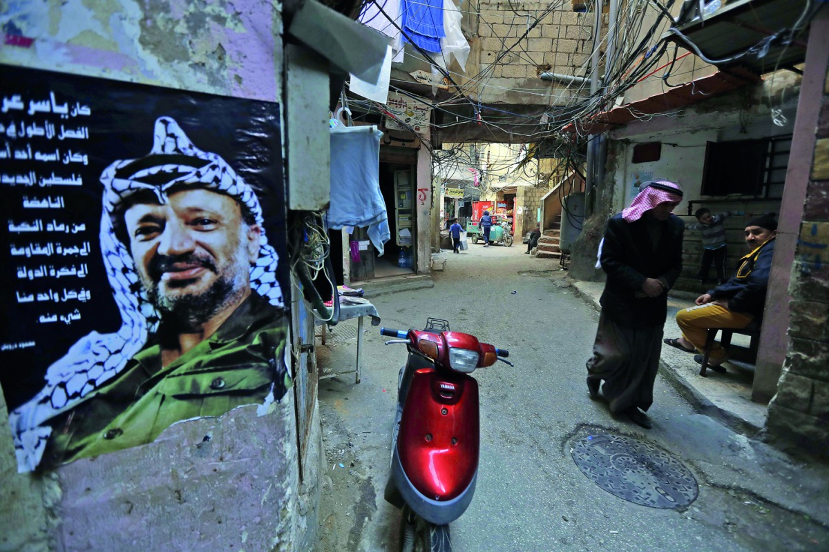 A Palestinian refugee walks at the Shatilla Palestinian refugee camp, on the southern outskirts of the Lebanese capital Beirut, yesterday. A poster showing late Palestinian leader Yasser Arafat is seen on the left. 