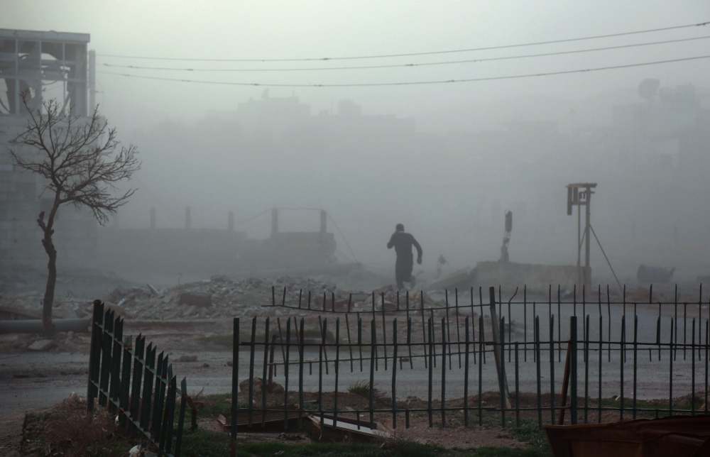 A Syrian man runs amidst smoke and dust in the rebel enclave of Eastern Ghouta on March 5, 2018 on the outskirts of Damascus.   AFP / HAMZA AL-AJWEH
