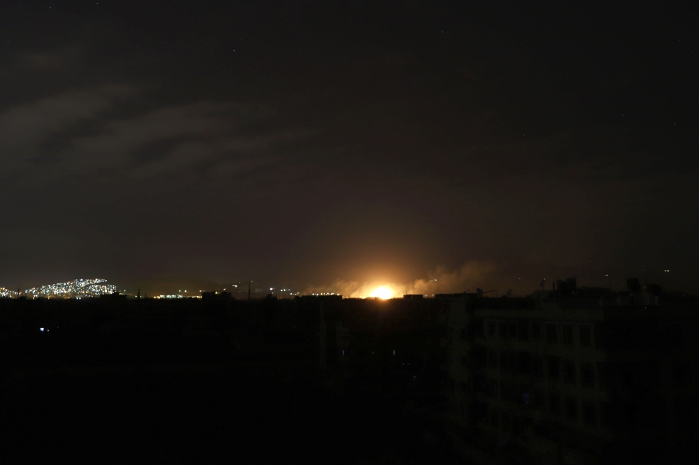 A picture taken late on March 10, 2018, shows an explosion, from a Syrian government air strike, illuminating the town of Arbin in the rebel-held enclave of Eastern Ghouta. AFP / AMER ALMOHIBANY
