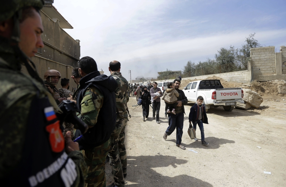 Russian and Syrian soldiers stand guard as Syrians from rebel-held Eastern Ghouta arrive at the regime-held checkpoint in Adra, on the northeastern outskirts of Damascus, after escaping the enclave through a corridor opened by the government forces on Mar