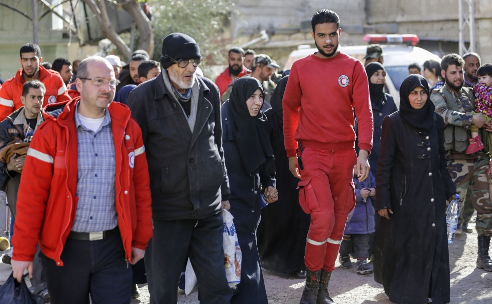 Members of the Syrian Red Crescent escort evacuated civilians from the rebel-held Eastern Ghouta enclave into the government side of the Wafideen checkpoint on the outskirts of the Syrian capital Damascus on March 14, 2018. / AFP / LOUAI BESHARA